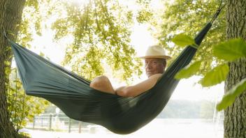 Senior man wearing straw hat relaxing in hammock at lakeshore model released Symbolfoto property rel