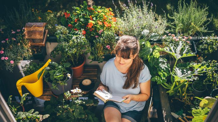 Woman sitting and reading book near plants in balcony model released, Symbolfoto, TILF00006
