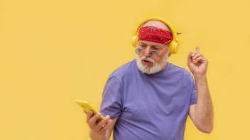 Senior man in headphones using smartphone Bearded senior man in casual outfit and headphones listening to music and brow
