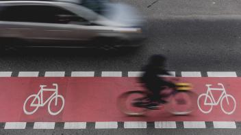 Ein Radfahrer faehrt auf einem markierten Radweg auf der Schlossstrasse und wird von einem Auto ueberholt in Berlin, 27.