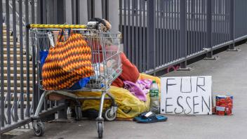 Ein Obdachloser sitzt mit seiner Habe an den Landungsbruecken in Hamburg auf dem Boden. Vor sich hat eine Dose und Schil