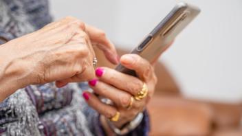 Elderly woman with smartphone, mobile phone in wrinkled female hands, close up. Concept of online co
