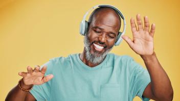 Happy mature african man dancing while listening to music with headphones against a yellow studio background. Carefree s