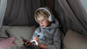 Boy wearing headphones using internet on smart phone in canopy at home model released, Symbolfoto property released, NJA