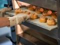 Eine Person schiebt in der Bäcker-Innung Berlin ein Blech mit Brötchen in einen Ofen.