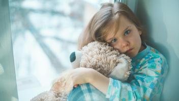 Ein Mädchen hält ihren Teddy fest im Arm und schaut traurig. 