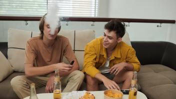 Young  men  smoking  electronic  cigarettes  at  home  when  having  pizza  with  beer Model Release