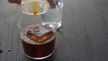 Making espresso tonic in tumbler glass, pour espresso over ice cube, wide photo Model Released Prope