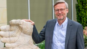 In Stein gemeißelt: Bürgermeister Otto Steinkamp neben der vor dem Wallenhorster Rathaus stehenden Skulptur „Stein des Anstoßes“, an der die Namen der bisherigen Preisträgerinnen und Preisträger zu sehen sind. 