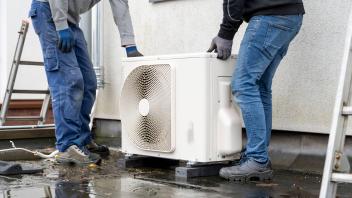 Two technicians installing an outdoor heat pump unit on a wet surface. panc03922 Copyright: xImageSourcex