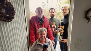 Sieglinde und Peter Tempel schauen von ihrer Haustür aus auf die defekte Kirchturmuhr (im Hintergrund) und den Turm des Museums „betont“. Dort stellt Museumsleiter Jan-David Mentzel (rechts) nun die Nussknacker des Ehepaares aus und verkauft diese. Das Geld fließt in die Reparaturarbeiten der Uhr. Pastor Sven Voß (2. von rechts) freut sich über die Aktion. 