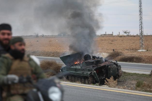 Syrische Oppositionskämpfer fahren an einem brennenden gepanzerten Fahrzeug der Regierung südlich von Hama vorbei.