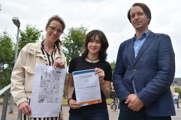 Melis Arslan (Mitte) Präsentierer Ihre Sieger-Urkunde Zwische Lehrerin Sara-Ann Simon und Schulleiter Kjell Pohns. 