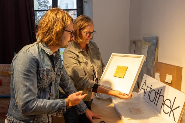 Artotheks-Mitarbeiterin Anne Haunhorst zeigt Benedikt Schlereth eines der Kunstwerke, die er sich ausgeliehen hat.
